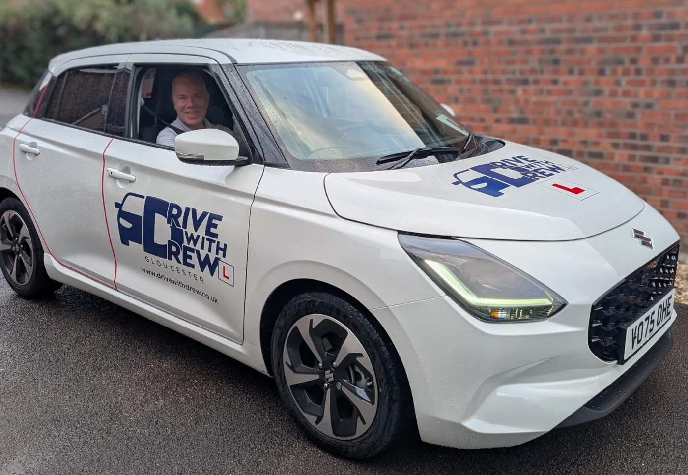 Drew in his branded white Suzuki Swift tuition car